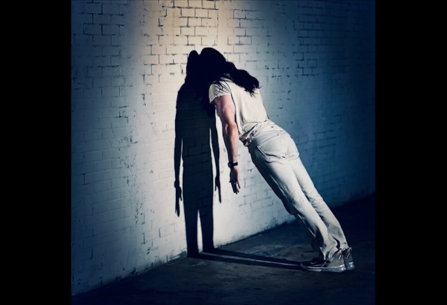 Andrew W.K. inclinado contra una pared bajo una luz fría en la imagen promocional de Temptation To Exist