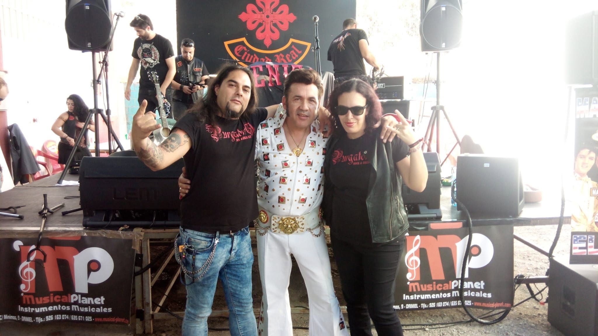 Marcos Elvis abrazado a dos músicos frente a un escenario