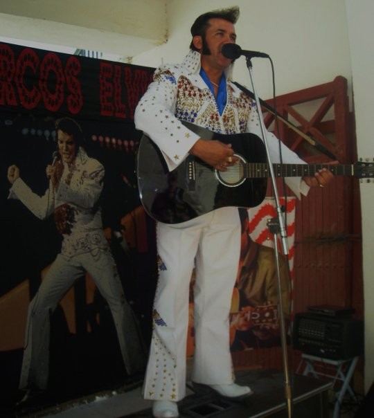 Marcos Elvis cantando con traje blanco y guitarra